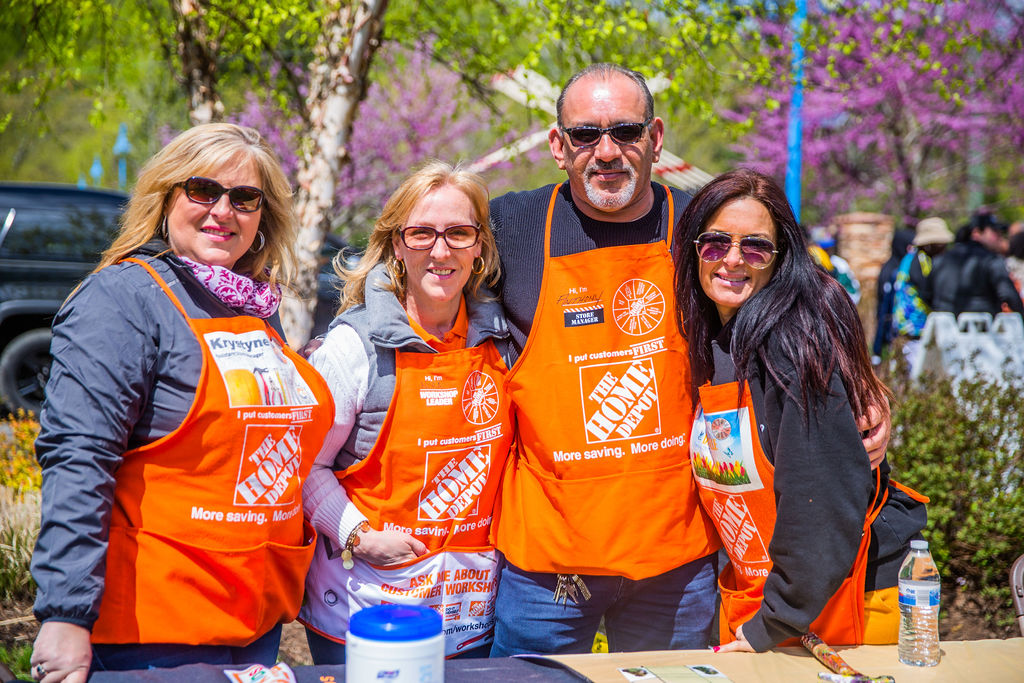 Four people standing together outdoors wearing orange Home Depot aprons.