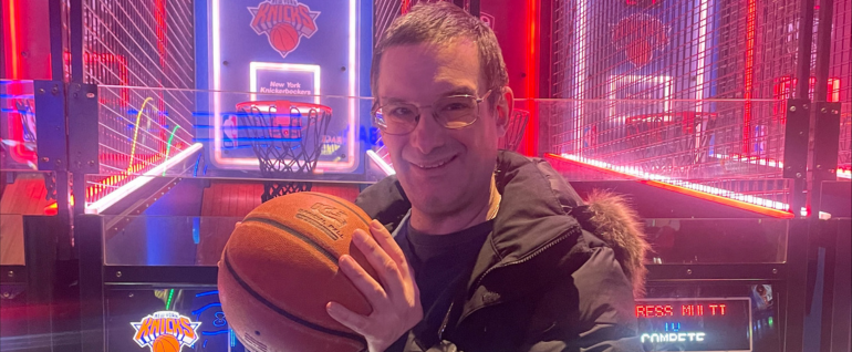 A man stands in front of a basketball arcade game, holding a basketball in his hands.