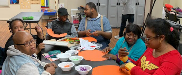 Six people sitting around a table working on a pumpkin craft.