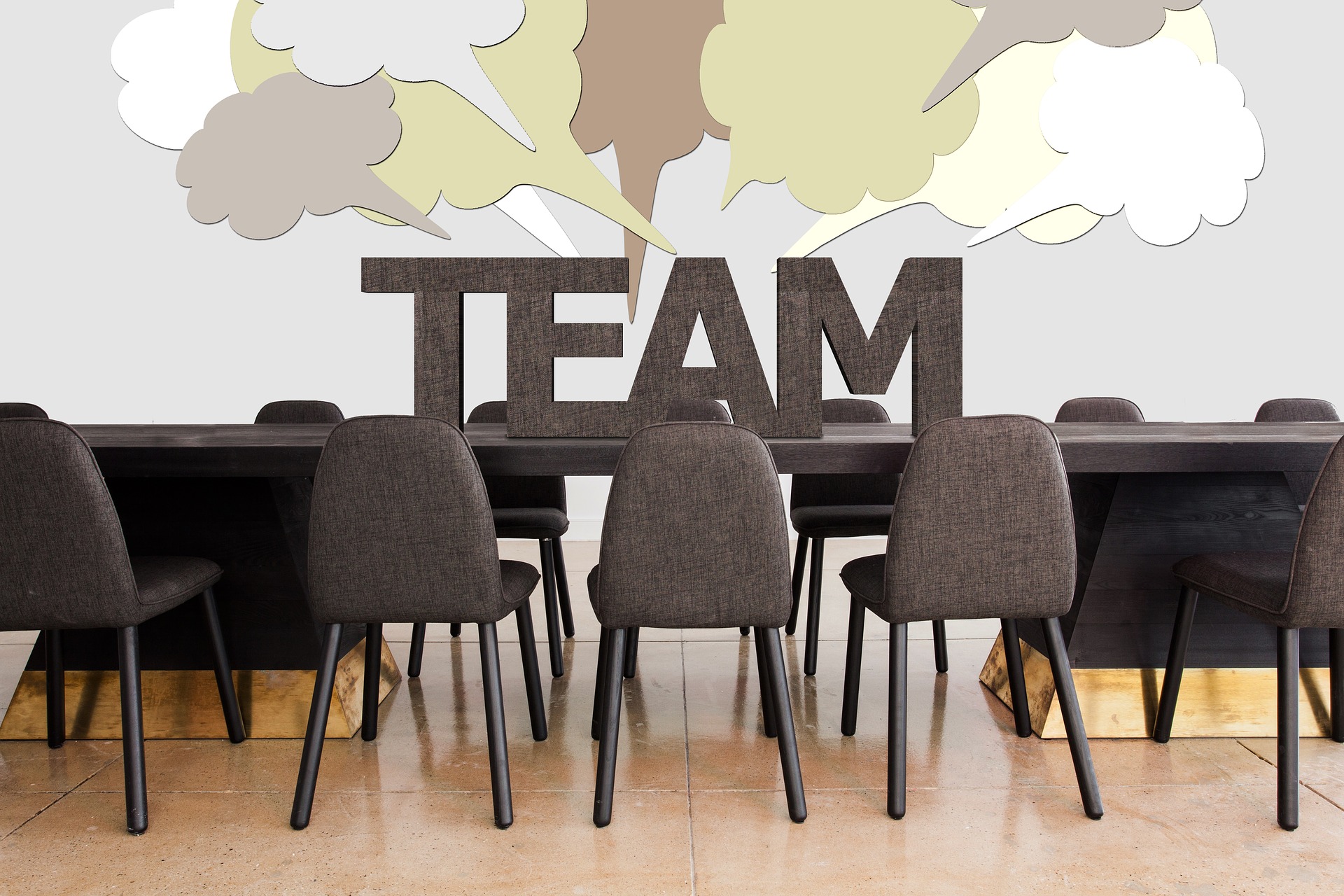 A board room table and chairs with the word TEAM on top, and text bubbles rising from the word TEAM.
