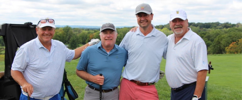 Four men in hats and polo shirts standing together on a golf course