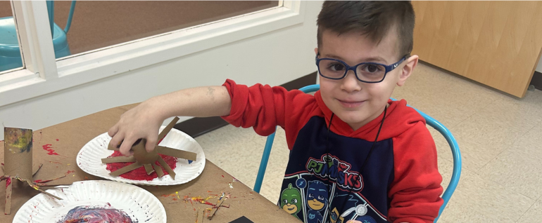 A boy sitting at a table working on a painting project.