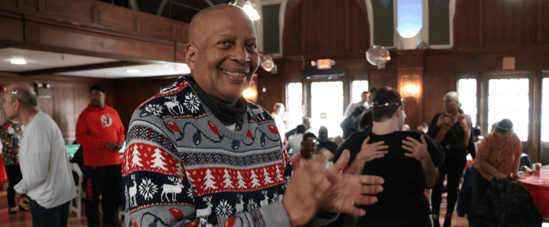 A man in a holiday sweater clapping at a party.