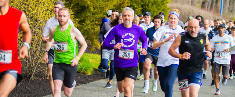 Runners in The Arc of Essex County's Building Tomorrows 5K. They are running on a path with greenery visible in the background.