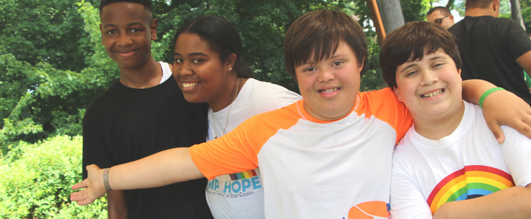 Three kids and a camp counselor standing together outside and smiling. Two of the people in the photos are wearing Camp Hope t-shirts.