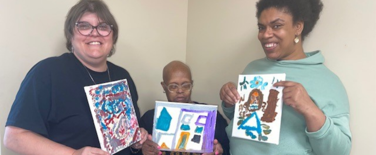 Three women holding paintings on canvases