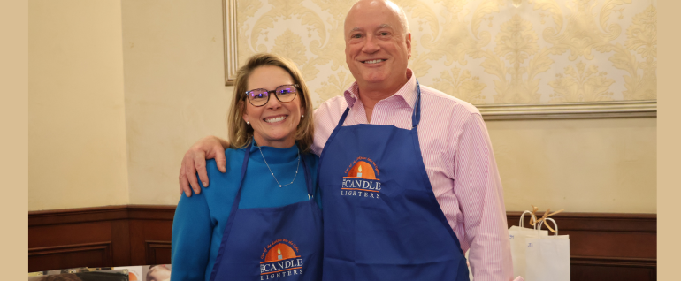 A woman and a man stand together wearing blue Candle Lighters aprons.