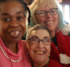 Three women in holiday attire smile together