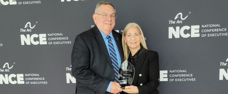 A man and a woman stand together, holding a glass award.