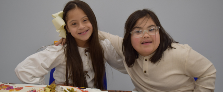 Two children sit at a Thanksgiving themed table together.