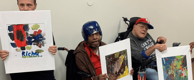Three men holding up paintings, each with a canvas border.