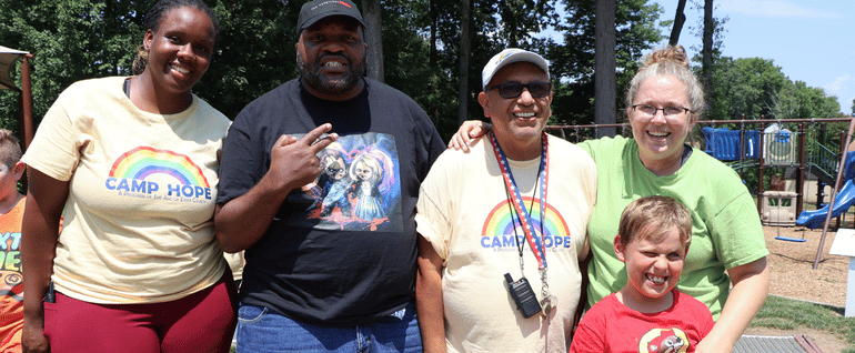 Four adults and a child stand together outdoors at Camp Hope.