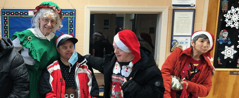 Three people in Santa hats standing near a woman dressed as Mrs. Claus.