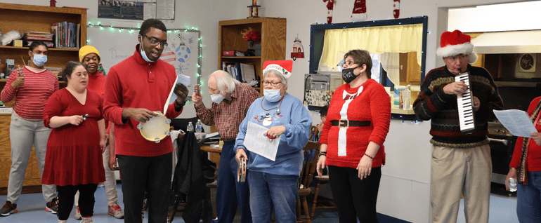 A group of people dressed in holiday attire and singing and playing instruments together.