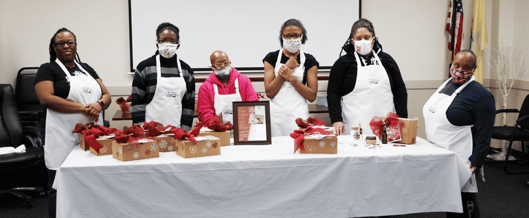 Six women wearing Studio Arc aprons and standing behind a table of winter-decorated cardboard boxes.