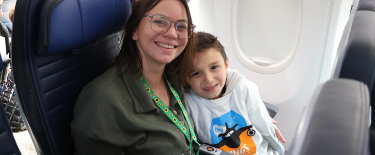 A woman and young boy sit in seats on a United aircraft, with the boy wearing a Wings for All t-shirt.