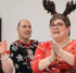 A group of five adults wearing holiday clothing and singing and clapping together.