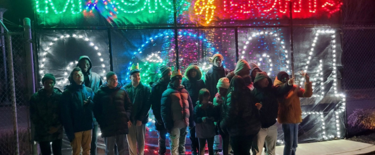 A group standing outdoors at night time in front of a "Magic of Lights 2024" light-up display.