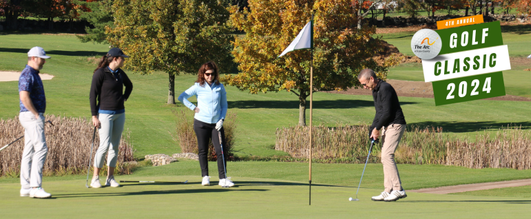 Four people on a golfing green with trees with autumn foliage behind them. The man on the right is putting a golf ball toward a hole with a flag. On the top right, The Arc of Essex County Golf Classic 2024 logo.