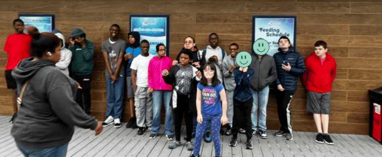 A group of children and teens standing outside an aquarium.