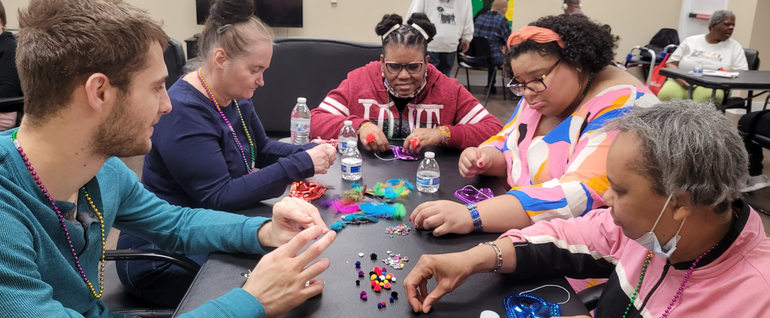 A group gathered making Mardi Gras masks around a table together.