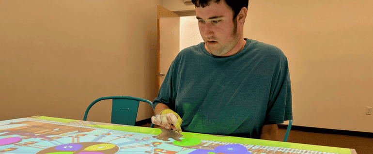 A teen boy sitting at an interactive Obie table, playing a virtual game.