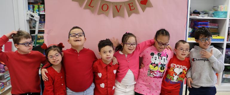 Stepping Stones students together wearing red and pink, under a "Love" sign.