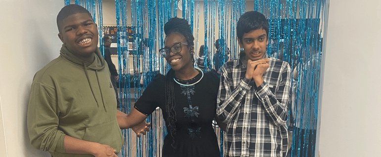 Two boys stand on either side of an Arc staff member at an Arc Children's Respite dance, with a sparkly backdrop.