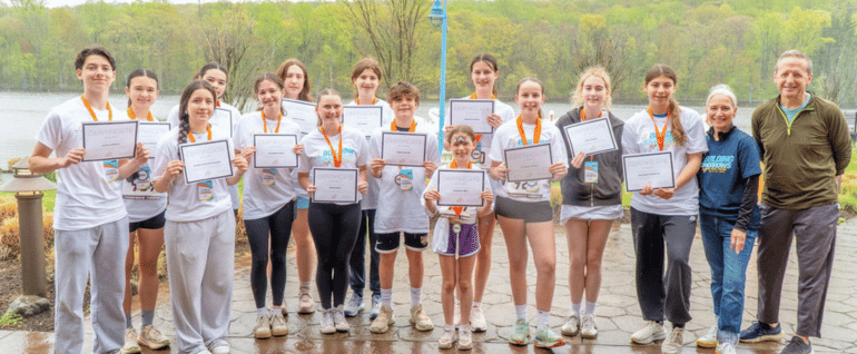A group of students poses in front of the reservoir at the South Mountain Recreation Complex, wearing Building Tomorrows shirts and holding certificates.
