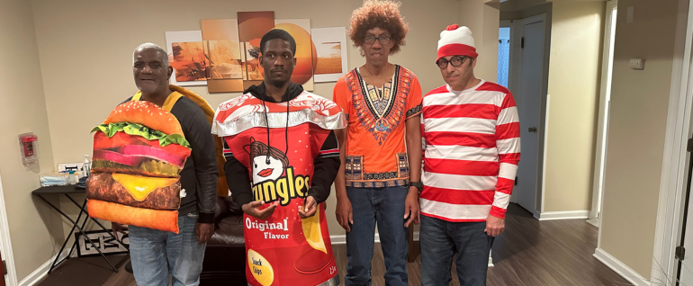 Four adult residents standing together in their Halloween costumes: (left to right) A cheeseburger, a Pringles can, a hippie, and Waldo in a red and white striped shirt.