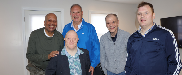 Four residents of the 45 Beechtree group home stand with West Caldwell Mayor Joe Tempesta (center, in a bright blue jacket) in the livingroom of their new home.