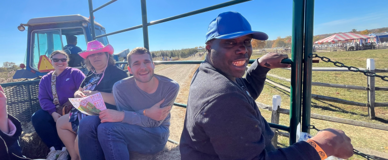 Four adults smiling and enjoying a hayride on a farm.