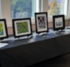 A row of framed artwork on a table with a black tablecloth at an art show.