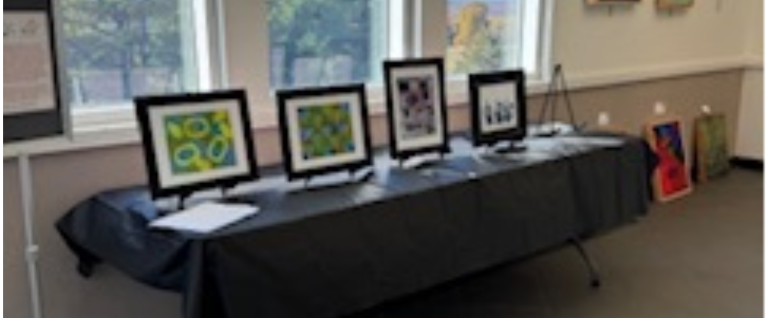 A row of framed artwork on a table with a black tablecloth at an art show.