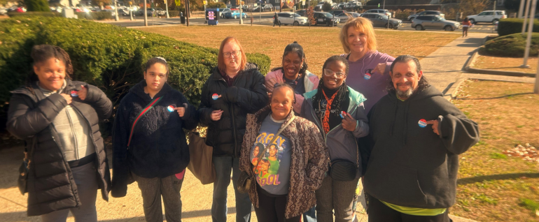 A group of seven people stand together, wearing "I Voted" stickers.