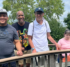 A group of four adults standing on a bridge amid a miniature golf course, overlooking a lake.