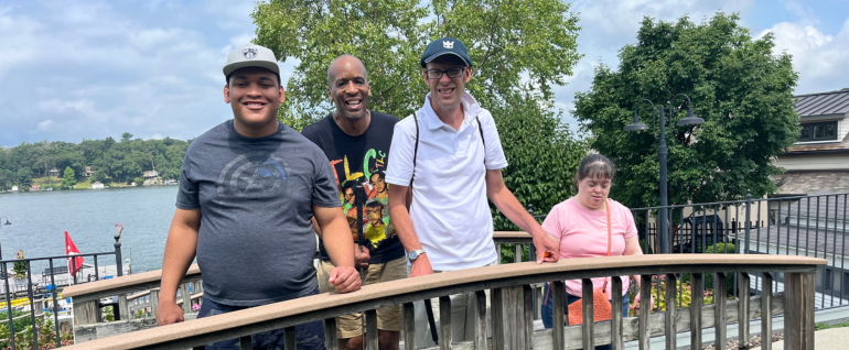 A group of four adults standing on a bridge amid a miniature golf course, overlooking a lake.