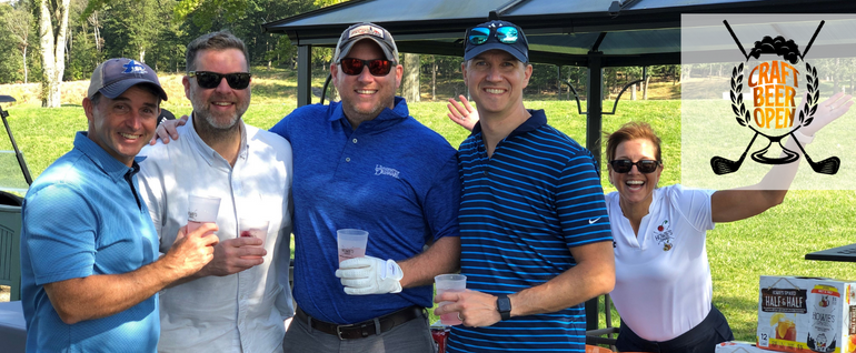 Four people standing together near a golf course with drinks in their hands. A woman smiling and lifting her arms to the right of them. Top right: Craft Beer Open logo.