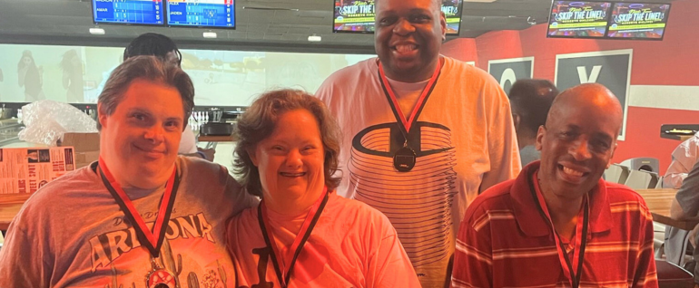 Four people standing in a bowling alley with medals hanging from their necks.