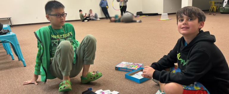 Two boys sitting on the ground playing a board game together.