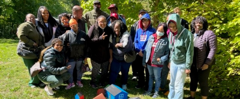 A group of 18 people standing together outside, with painted bird houses in front of them.