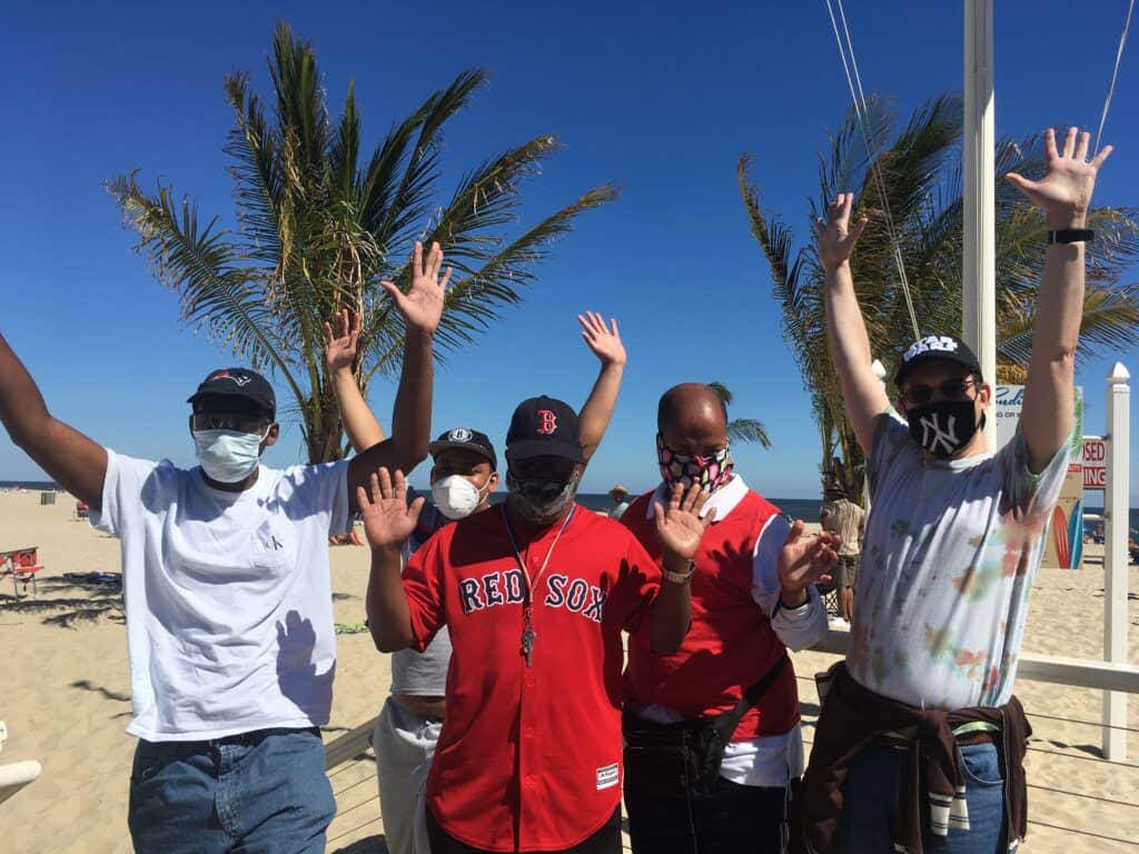 Five men standing on a beach with their arms in the air.