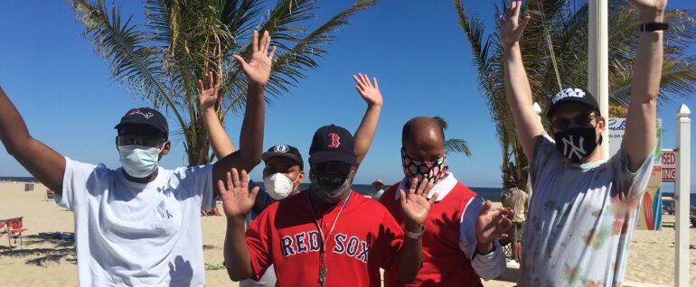 Five men standing on a beach with their arms in the air.