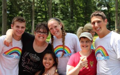 Seven people gathered together with their arms around each other's shoulders. They are outdoors, and three of the people pictured are wearing Camp Hope t-shirts.