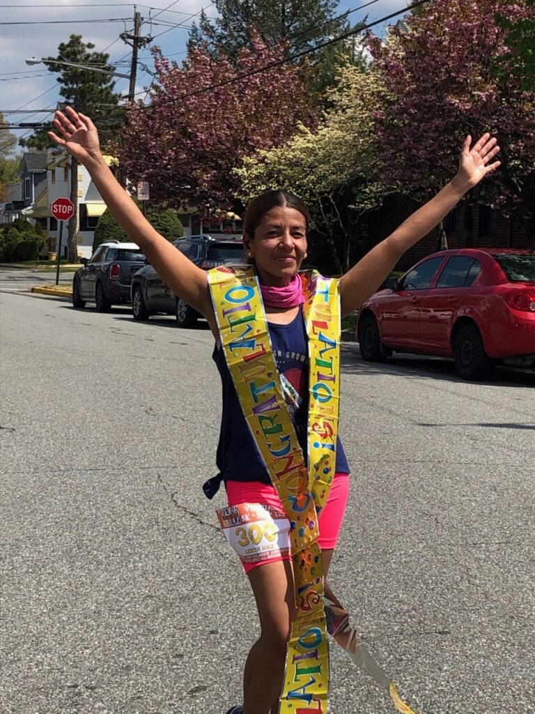 A woman running on a street with a runner's bib on her shorts and a 