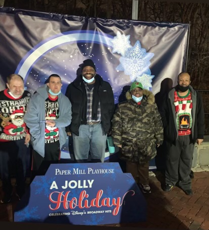 A group of people in holiday attire standing in front of a snow globe backdrop and in front of a sign that says 