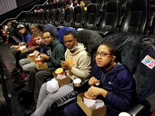 A group of people sitting in a row of a movie theater, holding popcorn and other snacks.