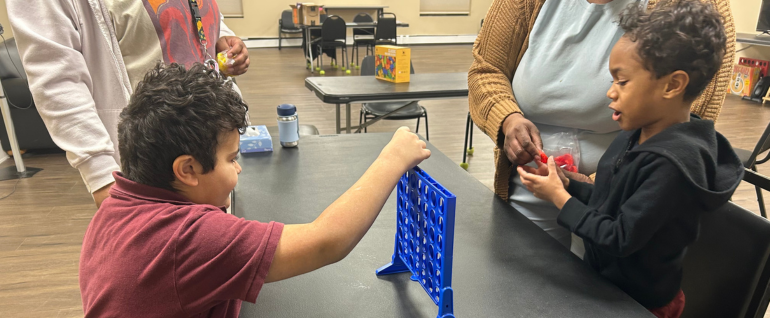 Two children playing Connect Four together at a table.