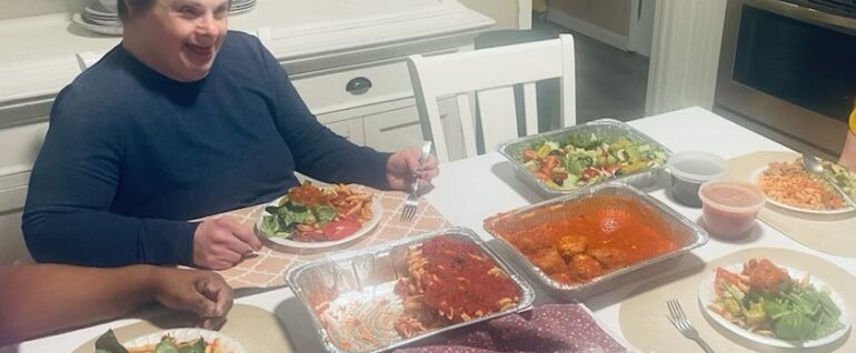 A woman sitting at a white table filled with trays of food, including pasta, meatballs, and salad.