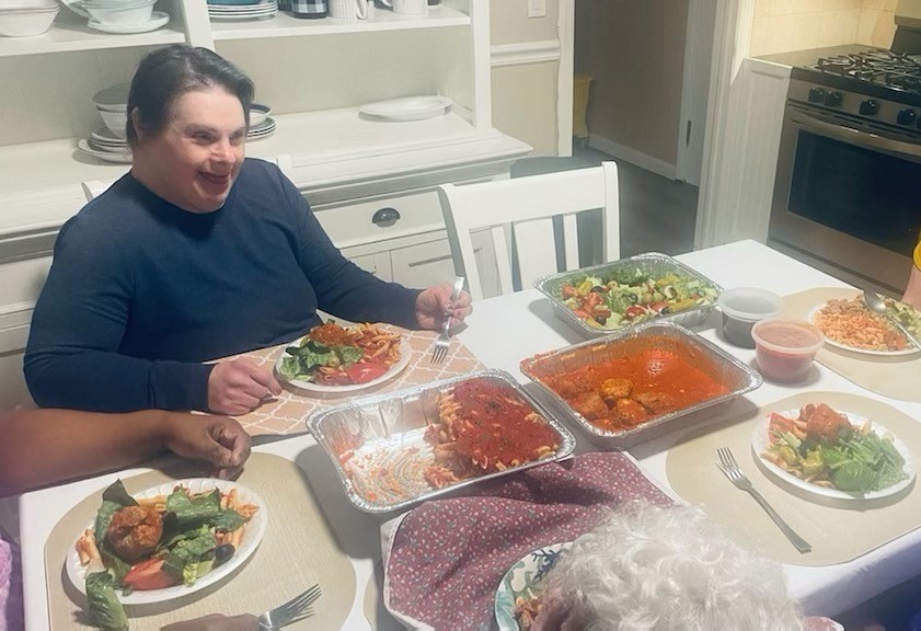 A woman sitting at a white table filled with trays of food, including pasta, meatballs, and salad.